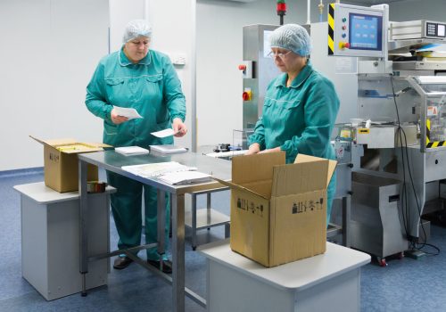 Pharmaceutical technicians work in sterile working conditions at pharmaceutical factory. Scientists wearing protective clothing